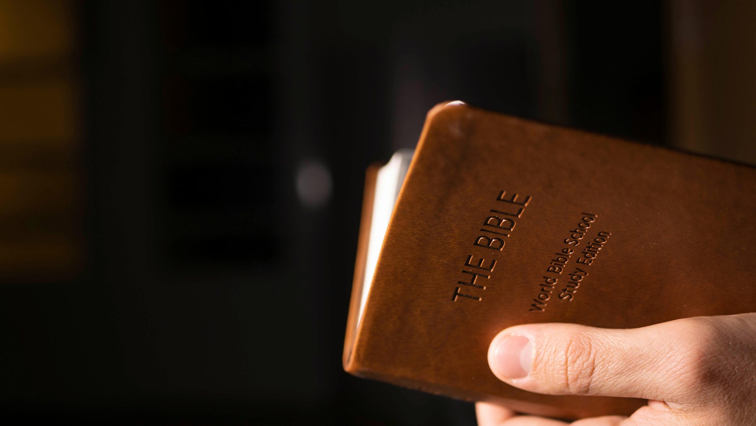Detailed view of a hand holding a leather-bound Bible indoors.